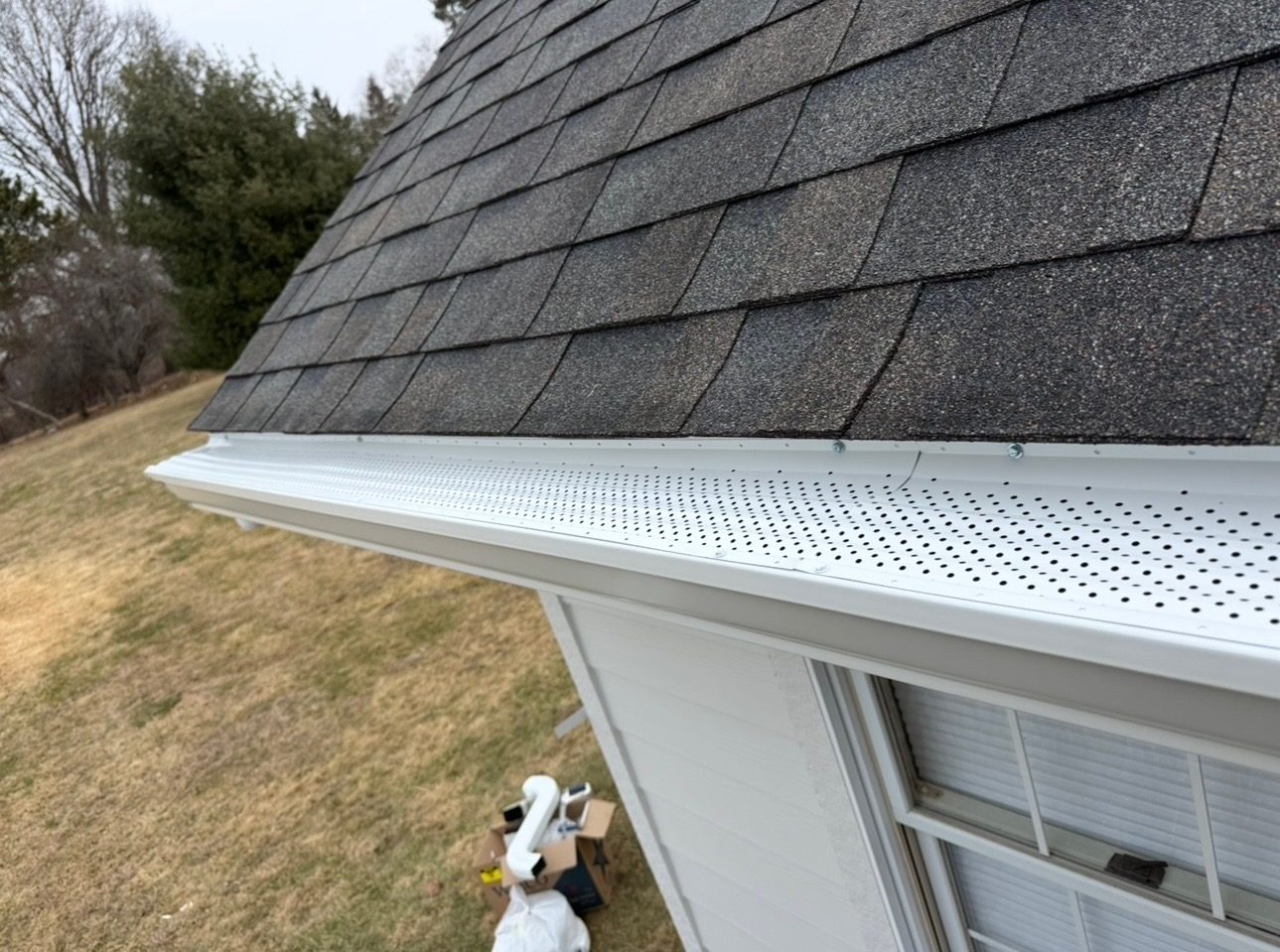 Installed white gutter guard detail along a shingle roof